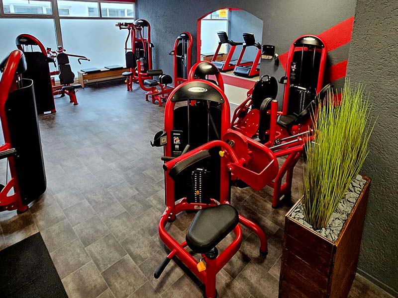Trainingsbereich im TWENTY FOUR SEVEN fit Beuna, Merseburg Trainingsbereich im Fitnessstudio TWENTY FOUR SEVEN fit in Beuna, Merseburg, mit zahlreichen Geräten für effektiven Kraftaufbau, grauen Wänden und modernem roten Design.
