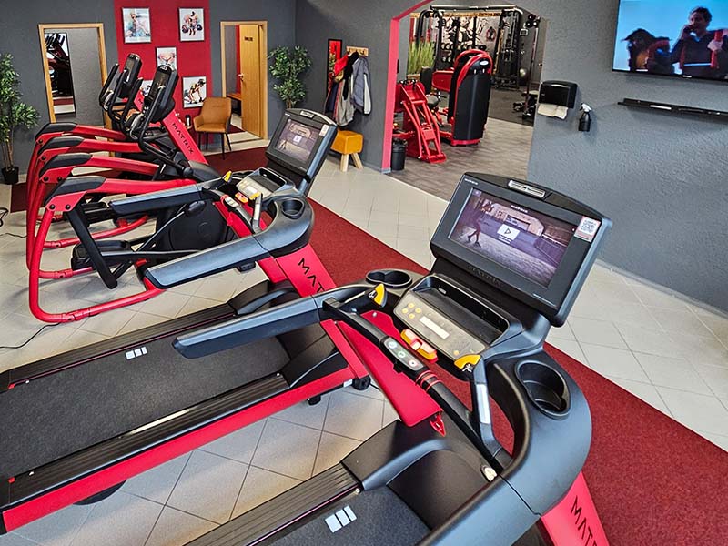 Cardiobereich im TWENTY FOUR SEVEN fit Beuna, Merseburg Moderner Cardiobereich im Fitnessstudio TWENTY FOUR SEVEN fit in Beuna, Merseburg, mit schwarz-roten Laufbändern und Steppern, grauen Wänden und stylischem roten Design.